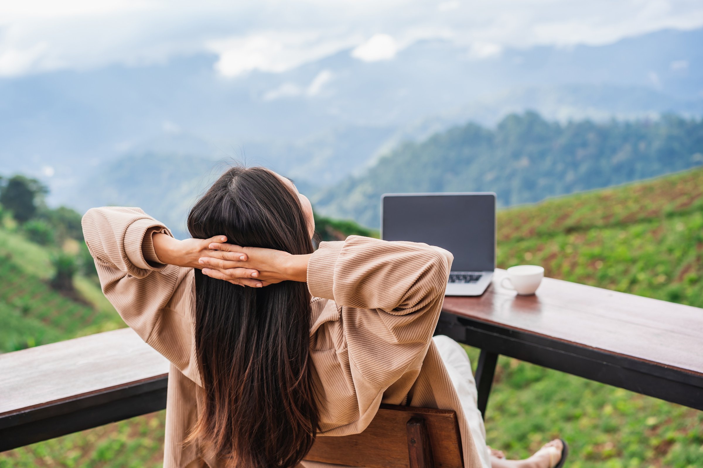 Young woman freelancer traveler working online using laptop and enjoying the beautiful nature landscape with mountain view